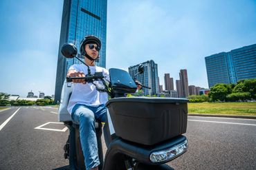 A man is riding a cargo electric scooter on a wide street
