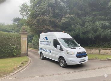 White Ford delivery van parked near a gated entrance with greenery.