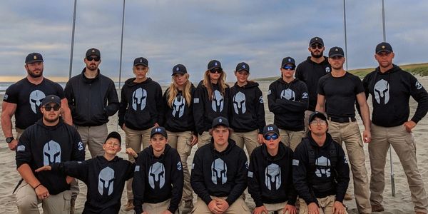 A group of people in matching Spartan hoodies and caps posing on a beach.
