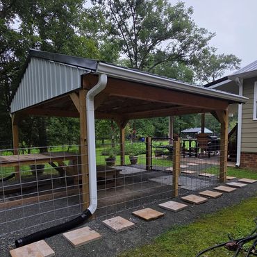 Outdoor wooden pavilion with metal roof and stepping stones.