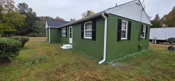 Green-painted single-story house with white gutters in a grassy yard.