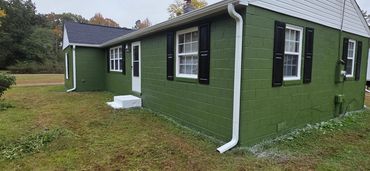 Green-painted brick house with white trim and black shutters on a grassy lawn.