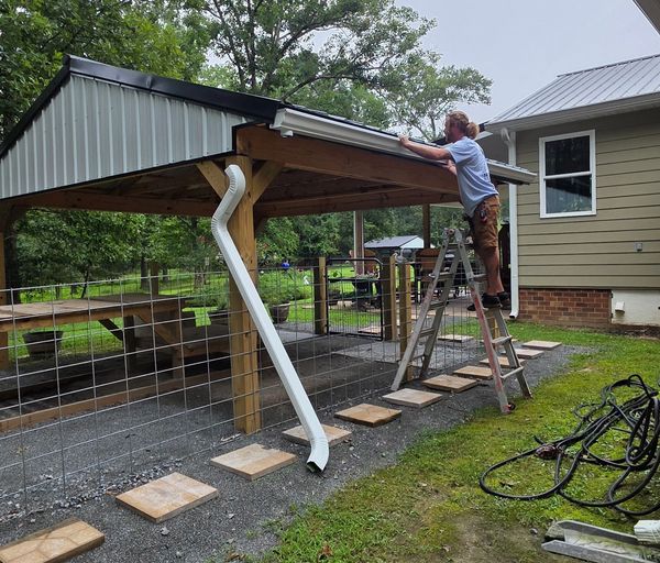 Man working on a metal roof of a wooden structure using a ladder.