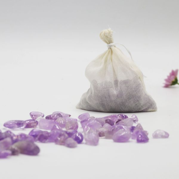 A white fabric bag with loose Amethyst crystals in-front of the bag