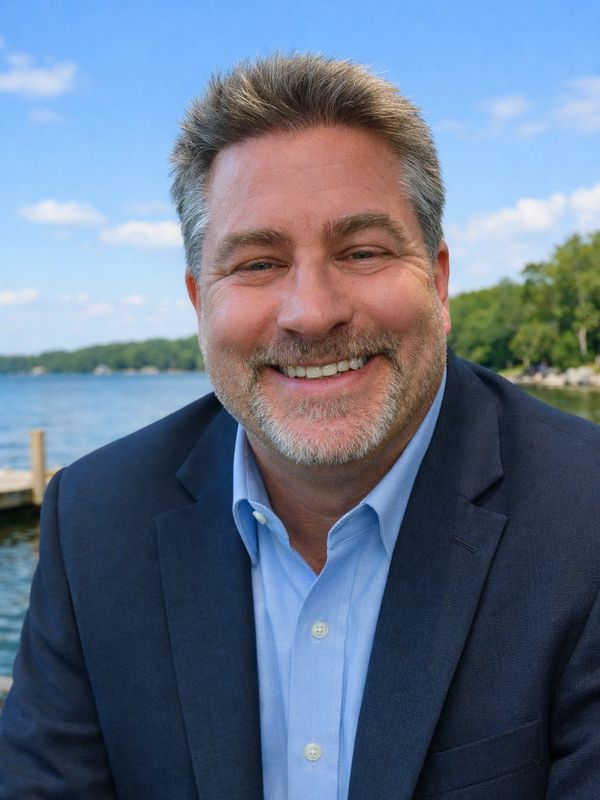 Smiling man in a suit by the lakeside on a sunny day.