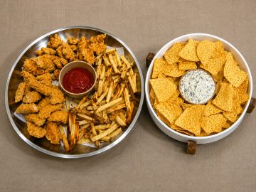 Two platters with fried chicken, fries, chips, and dips.