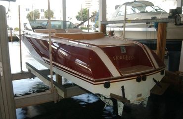 A red and white boat with 'TUSCANY' on the side on a boat lift.