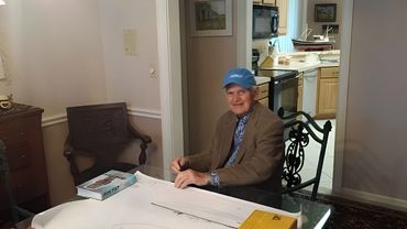 A man in a blue hat and suit signing a document at a desk.