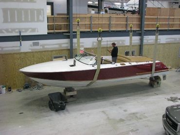 A red boat on a small trailer outside a building.