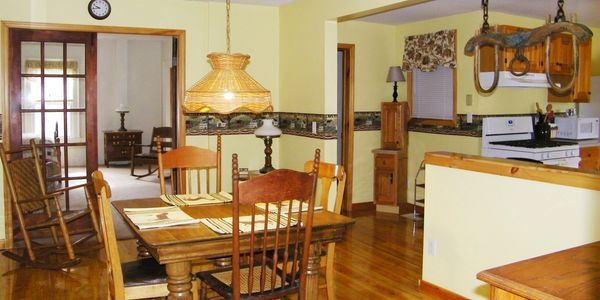 Dining room with full vintage dining table, knotty pine floors. Looks into kitchen and living room