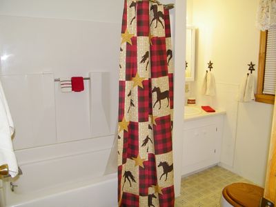 Picture shows full downstairs bath with shower, tub, and red and black plaid horse shower curtain