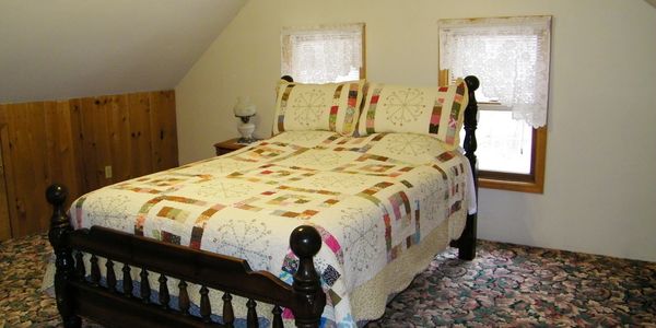 Upstairs master bedroom with pretty quilted queen bed, sloped ceiling, and two windows