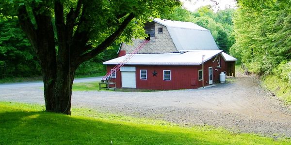 Picture shows red dairy barn with additional driveway parking and trees in in the background