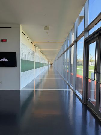 Long, modern hallway with large windows overlooking a sports field.