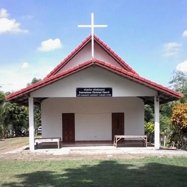 Small Christian church with a red roof and white cross under a blue sky.