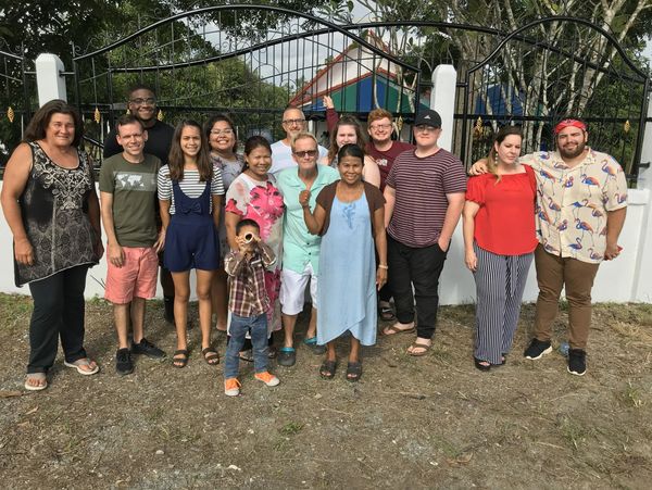 A diverse group of people posing happily outdoors in front of a gated entrance.