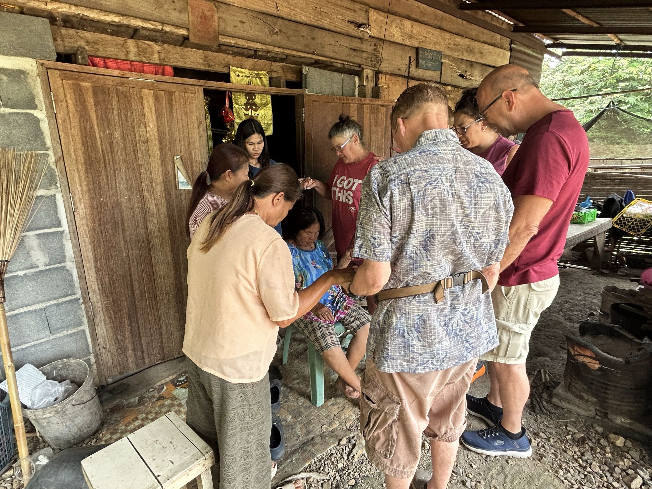 A group of people gathered around a seated woman in a rustic setting.