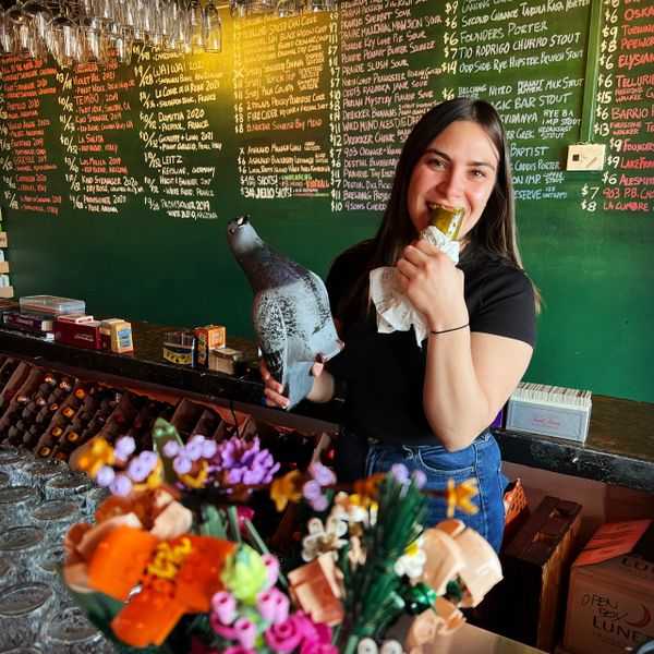 Bartender Gretchen holding a plastic pigeon and eating a giant pickle
