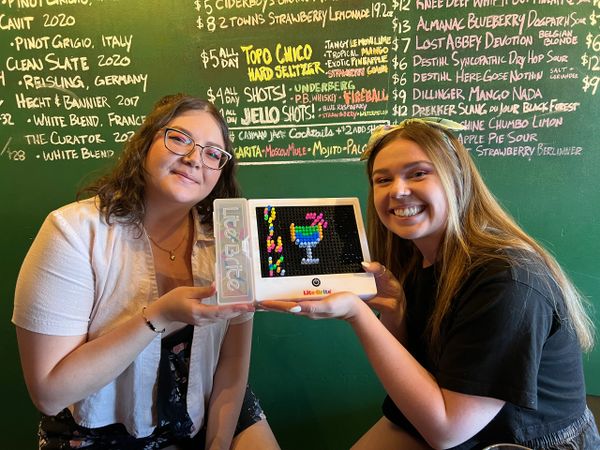 Two guests creating a picture on a Lite Brite (Light Bright) that says "OINK"