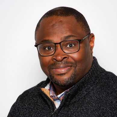 Smiling man wearing glasses and a dark sweater against a white background.