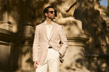 Man in beige plaid blazer and sunglasses posing outdoors in warm sunlight.