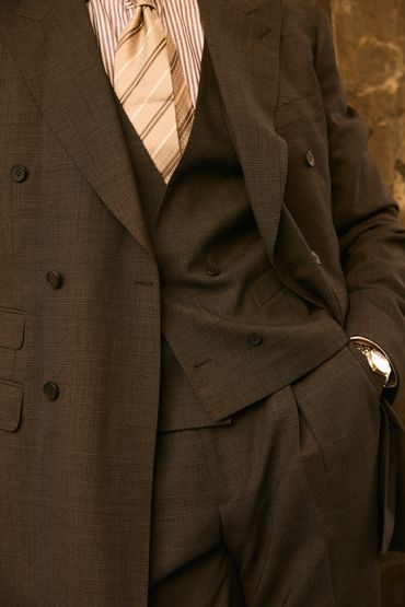 Man wearing a brown plaid suit with a beige striped tie and a watch.