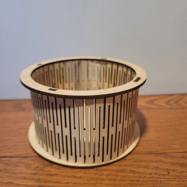 Wooden cylindrical model with vertical slits on a wooden surface.