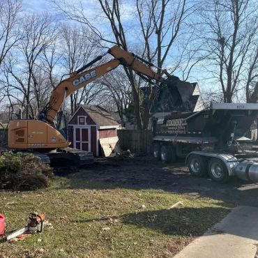 Excavator loading debris into a dump truck in a residential yard.