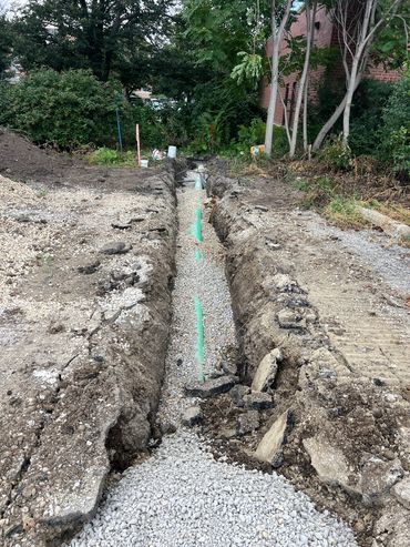 Trench with a green pipe and gravel for drainage or utilities.