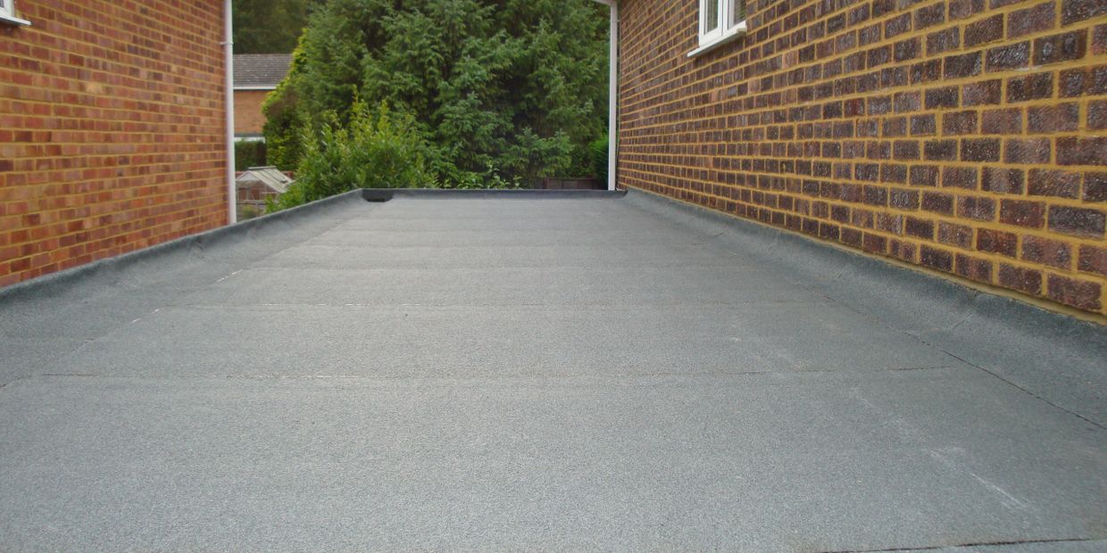 A flat roof between two brick walls with trees in the background.