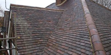 Old house roof with weathered brown tiles and a ridge line.