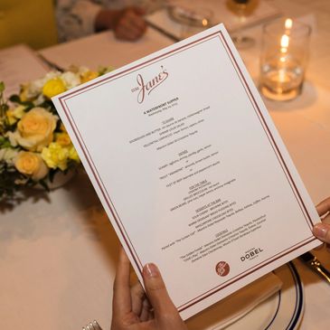 Person holding a detailed dinner menu at a formal table setting with flowers and candlelight.