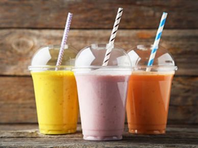 Three colorful smoothies in plastic cups with straws on a wooden surface.