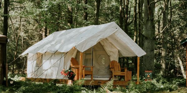 Cozy canvas tent with wooden chairs in a forest setting.