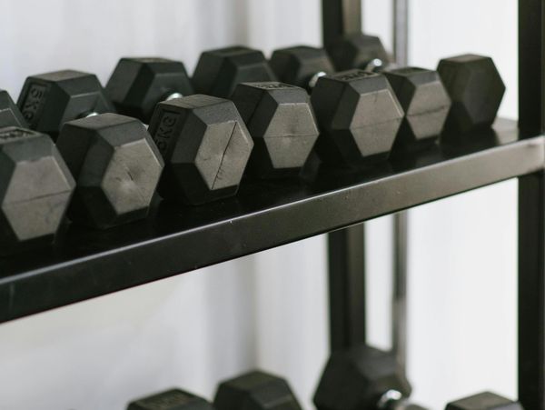 Black hexagonal dumbbells arranged on a metal rack in a gym.