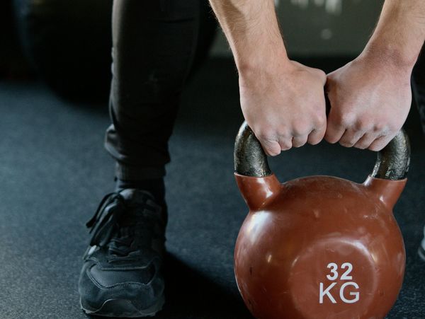 Person gripping a 32 kg kettlebell on gym floor.
