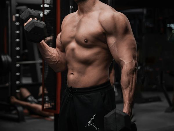 Muscular man lifting dumbbells in a gym, showcasing defined muscles.