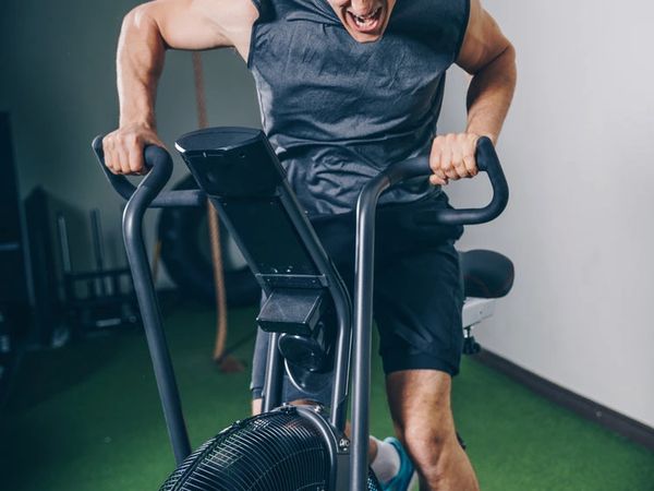 Man intensely working out on an air bike in a gym.