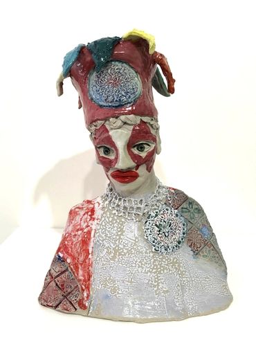 a figurative ceramic sculpture with decorated face and bust and a coloured party style hat