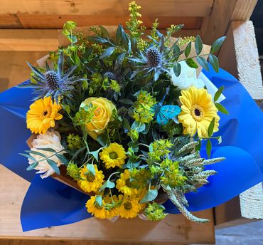 Bright floral bouquet with yellow flowers, greenery, and a blue butterfly accent.
