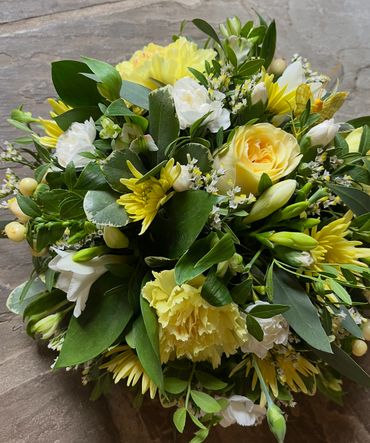 A vibrant bouquet of yellow and white flowers with lush green leaves.