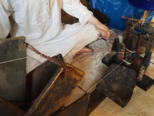 Person in white traditional clothing weaving on a wooden loom.