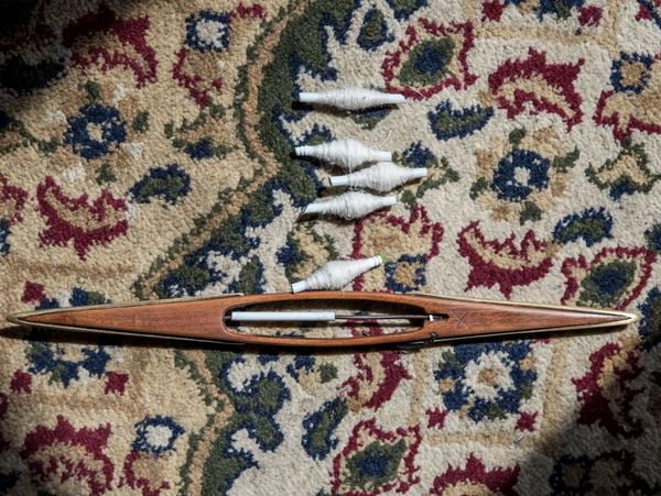 A wooden weaving shuttle and bobbins on a patterned rug.