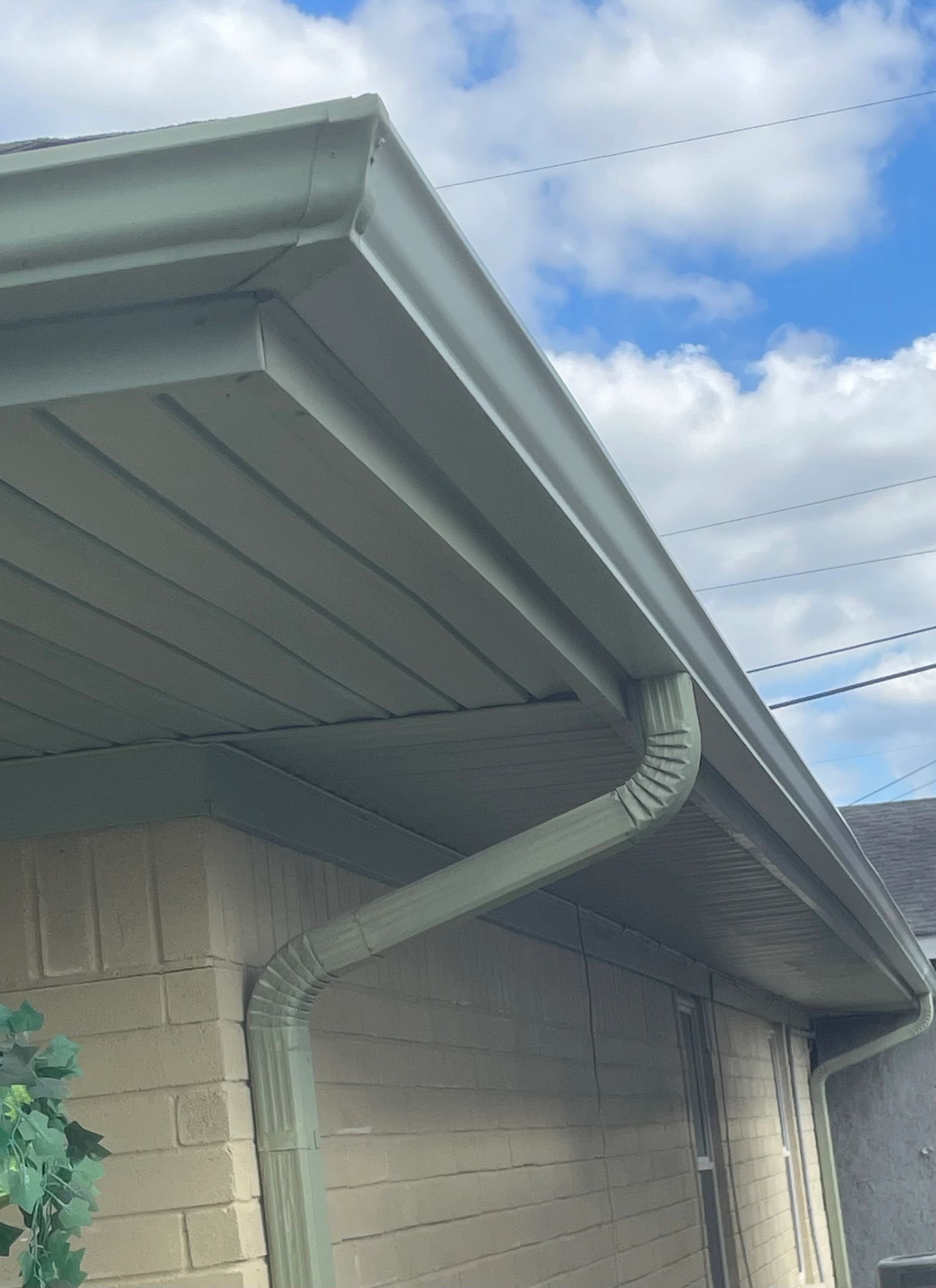 Close-up of a house gutter system against a partly cloudy sky.