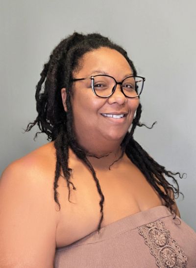 Smiling person with glasses and dreadlocks.