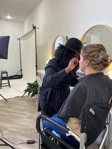 Makeup artist applying makeup to a seated woman with an elegant hair accessory.