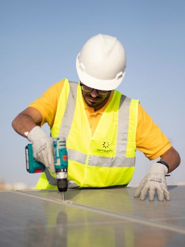 an electrical engineer wearing a helmet and a vest is drilling a solar panel