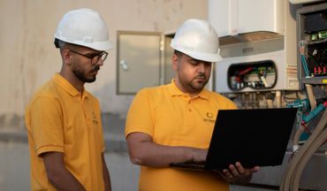 engineers wearing helmets and holding laptop and standing in front of an inverter
