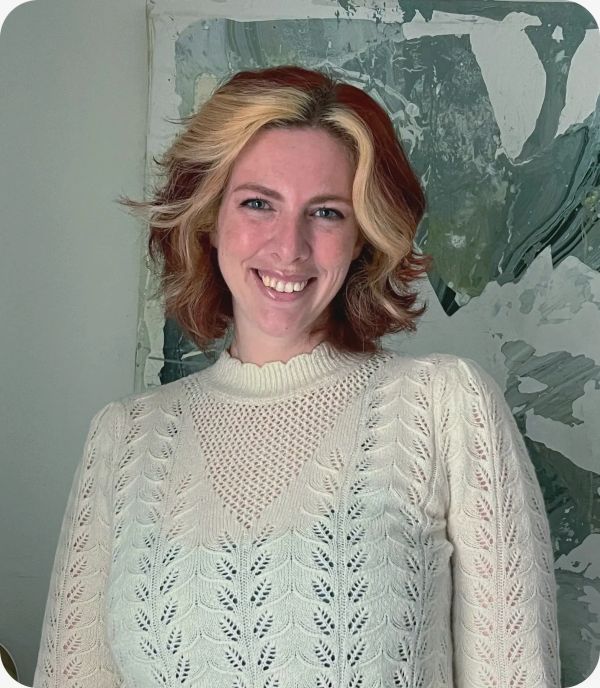 Woman smiling with red and blonde hair in a white knit sweater.