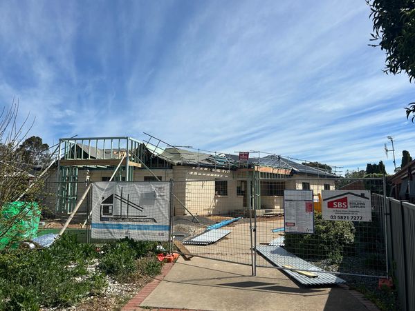 Residential building under construction behind a fenced area on a sunny day.